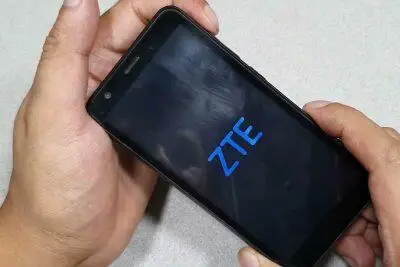 Manos sosteniendo un teléfono ZTE con el logotipo de ZTE en la pantalla. Desbloqueo del teléfono ZTE.